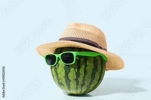 Watermelon with sunglasses and straw hat on green pastel background
