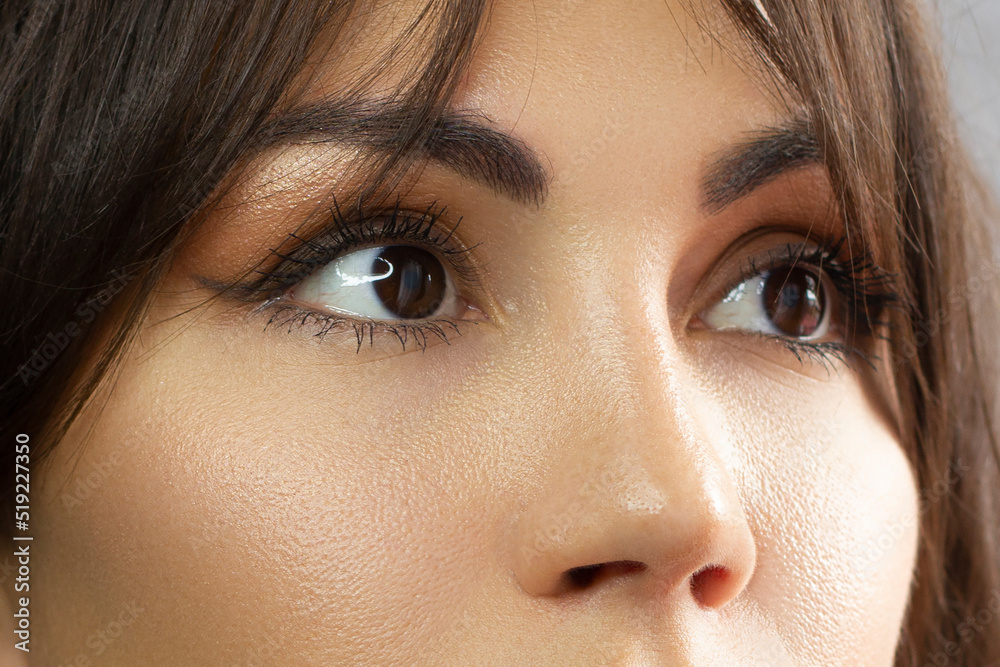 Fototapeta premium Glamour close-up portrait of beautiful woman model face with winged black eyeliner make-up, clean skin on white background. Long eyelashes and thick eyebrows.