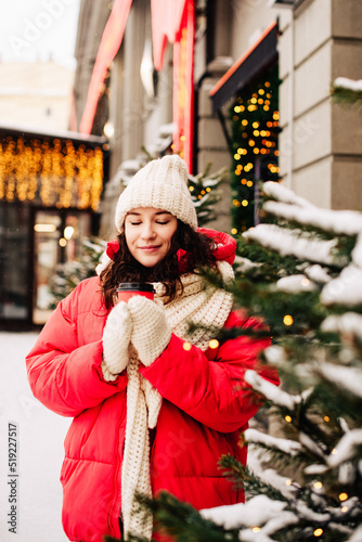 Young pretty brunette woman in red jacket, white hat, scarf and mittens with cap of coffee to go © Denira