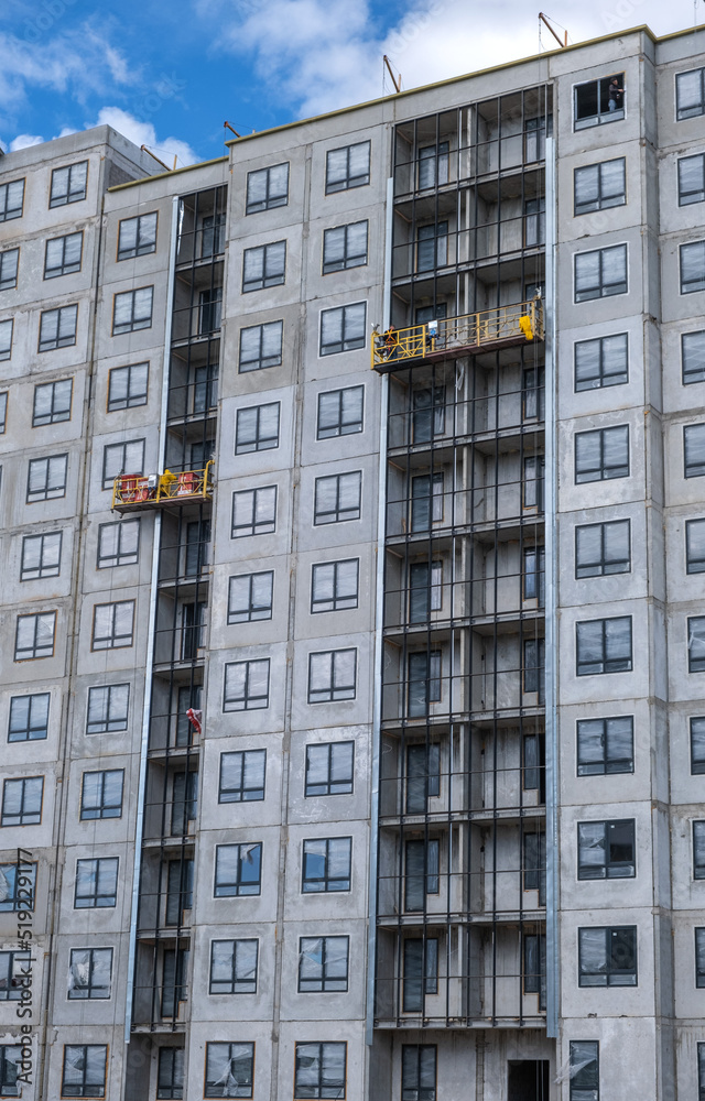 Builders, installers, high-rise workers, industrial climbers, plasterers on the lift, cladding of the facade of the building, completion of the construction of a residential building