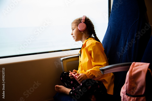 A girl in headphones on a train looks out the window. Journey.