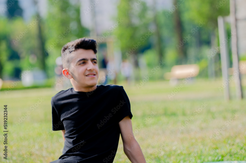 Handsome young boy in black shirt. Happy young male smiling on the grass in the park. Handsome young boy in black shirt. Happy young male smiling on the grass in the park.
