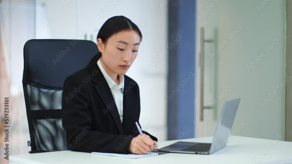 Young focused asian businesswoman studying document on laptop and writing notes, working at her office, free space Young focused asian businesswoman studying document on laptop and writing notes, working at her office, free space