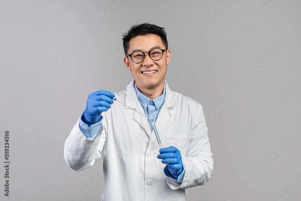 Smiling mature japanese guy doctor in white coat, glasses with stethoscope in rubber gloves hold test for covid-19 virus