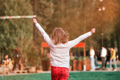 A 10-12 year old girl runs hopping around the park with her arms raised. A happy child enjoys life. Positive emotions, happy childhood.