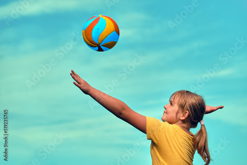 A girl is playing volleyball . The child hits the ball with his hand . Outdoor play