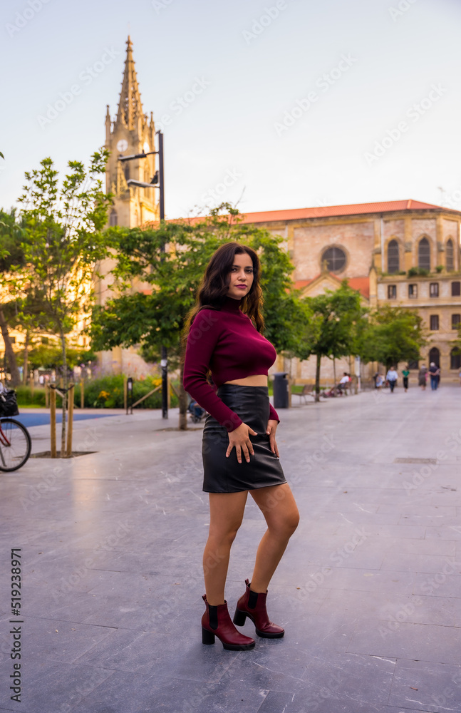 A brunette woman with a leather skirt next to a church, lifestyle in the city