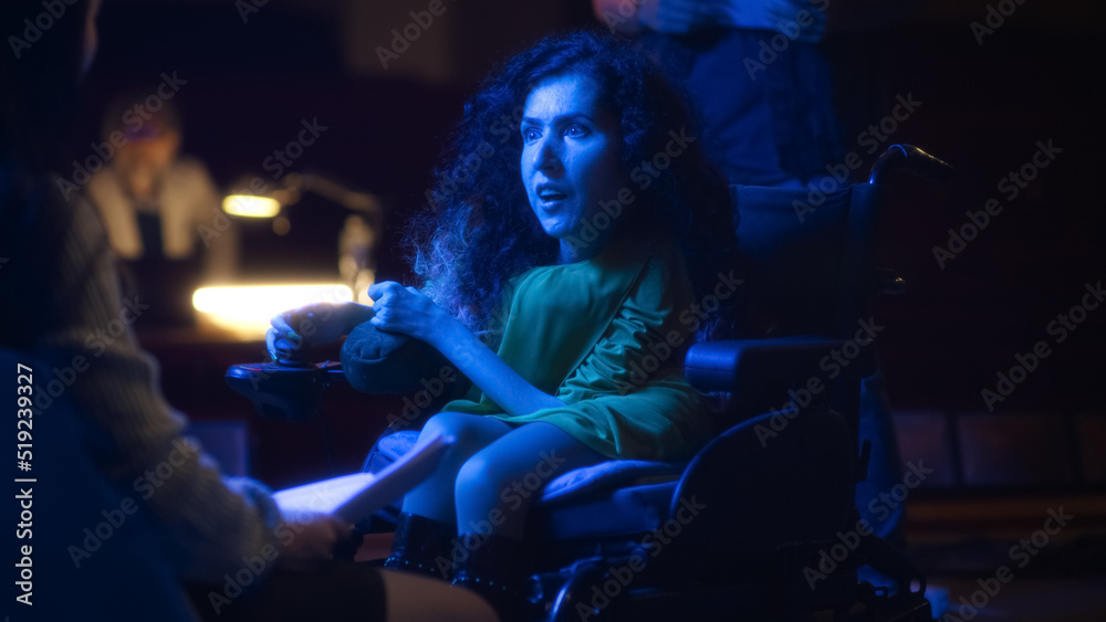 Actress with disability in play rehearsal emotionally acting in wheelchair on theater stage with a group of actors and director