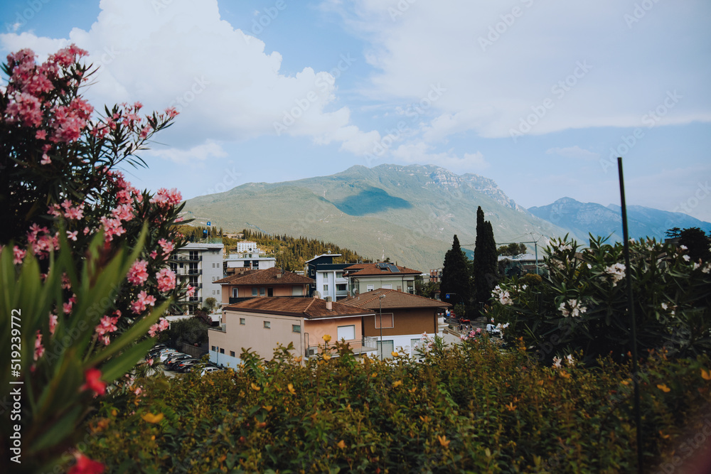  Riva del Garda. Houses and architecture of the city against the backdrop of mountains. Beauty and vacation, summer day, travel, flowers and city view.