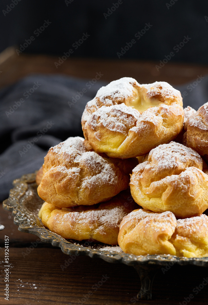 Baked eclairs with custard cream on a metal round plate sprinkled with powdered sugar