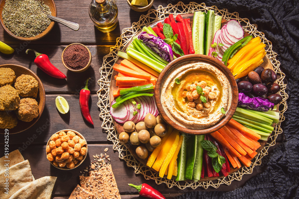Arabic Cuisine;  Middle Eastern Hummus platter with assorted snacks. Hummus dip with fresh vegetables sticks, falafel, chickpeas, pita bread,olive oil and whole grain crackers. Top view with close up. - obrazy, fototapety, plakaty 