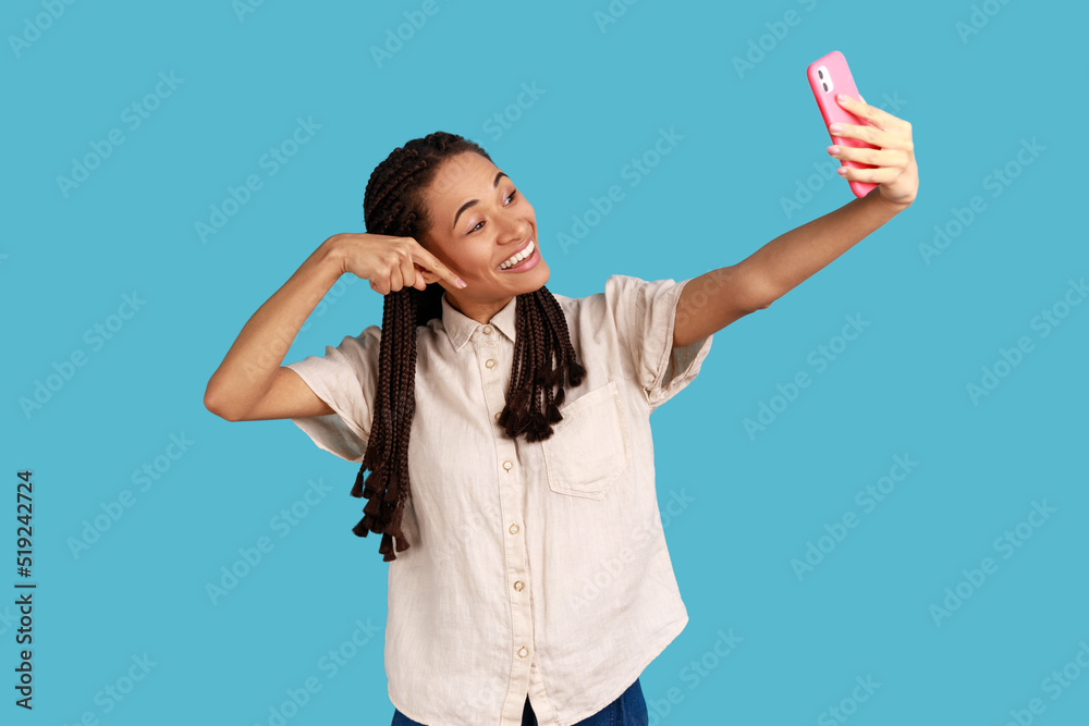 Look down, subscribe. Cheerful woman blogger making video call or online streaming, using phone, pointing finger down, asking to follow social media. Indoor studio shot isolated on blue background. Look down, subscribe. Cheerful woman blogger making video call or online streaming, using phone, pointing finger down, asking to follow social media. Indoor studio shot isolated on blue background.