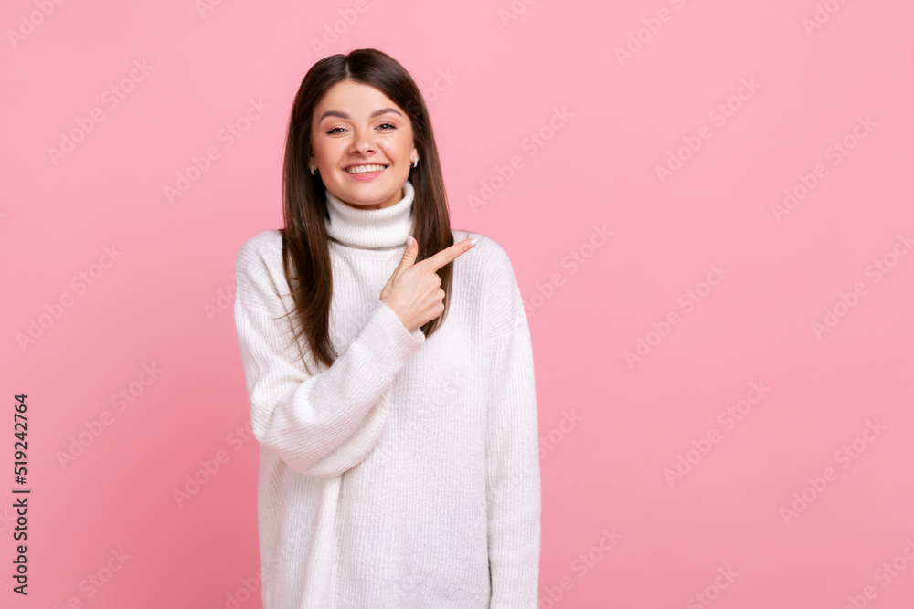 Charming young girl pointing aside at empty place for ad content, copy space for commercial product, wearing white casual style sweater. Indoor studio shot isolated on pink background. Charming young girl pointing aside at empty place for ad content, copy space for commercial product, wearing white casual style sweater. Indoor studio shot isolated on pink background.
