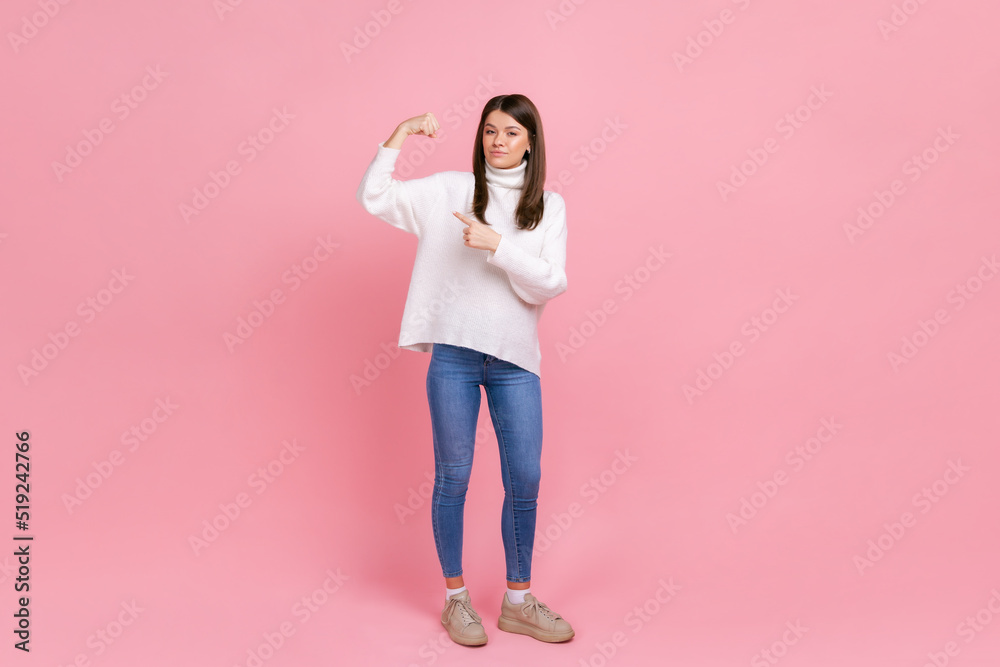 Full length portrait of energetic woman raised hands showing biceps, expressing power, female right, wearing white casual style sweater. Indoor studio shot isolated on pink background. Full length portrait of energetic woman raised hands showing biceps, expressing power, female right, wearing white casual style sweater. Indoor studio shot isolated on pink background.