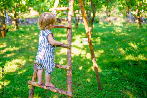 A little girl climbs a wooden ladder. A brave child is not afraid of heights. Striving upward, growth and development
