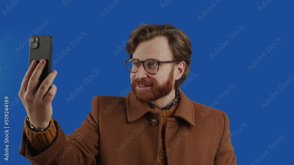 Stylish red hair ginger bearded man talking over the smartphone videocall - blue screen chroma key background. High quality 4k footage Stylish red hair ginger bearded man talking over the smartphone videocall - blue screen chroma key background. High quality 4k footage