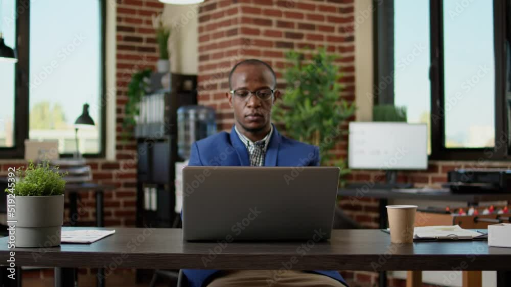 Portrait of african american employee answering email on laptop, working on website report. Office entrepreneur analyzing paperwork research on computer, doing internet research.