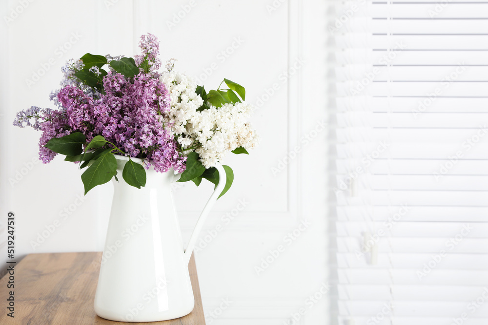 Fototapeta premium Beautiful lilac flowers in vase on wooden table near white wall. Space for text