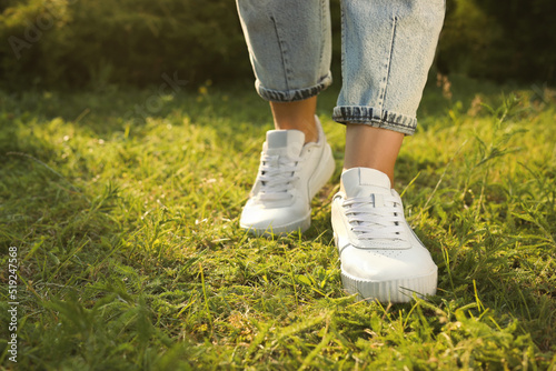 Woman in jeans and white shoes walking on green grass, closeup. Space for text