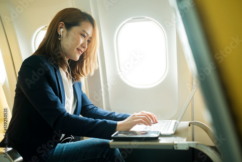 Business woman In a plane  works on using laptop computer and phone