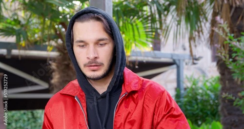 Suspicious-looking young man in hoodie is stirring up something illegal, so he looks around nervously, front view. Guy rubs his nose like drug addict after another snuffed dose photo