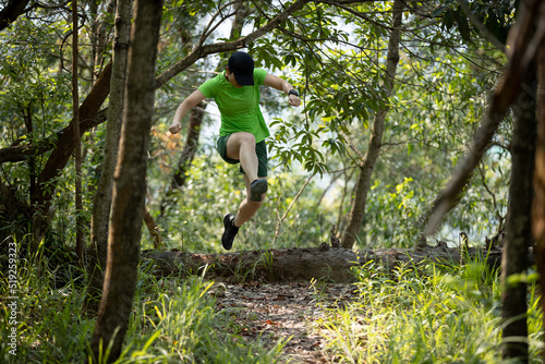 Woman trail runner running and jumping over a fallen tree in tropical forest mountain