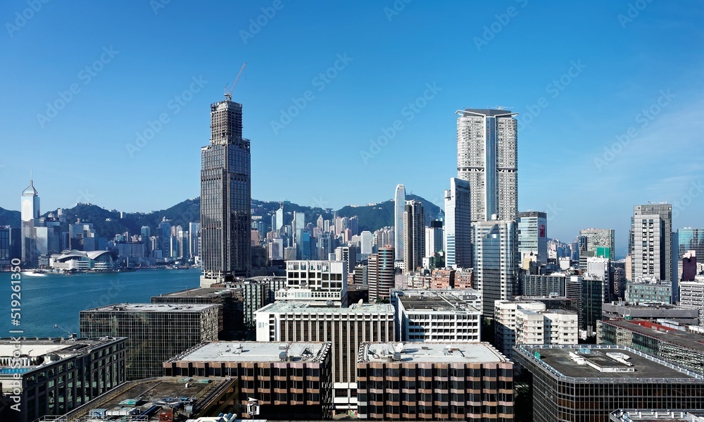 Scenery of Hong Kong, viewed from Tsim Sha Tsui area in Kowloon, with city skyline of crowded skyscrapers along Victoria Harbour under blue clear sky ~ Beautiful cityscape of Hongkong on a sunny day