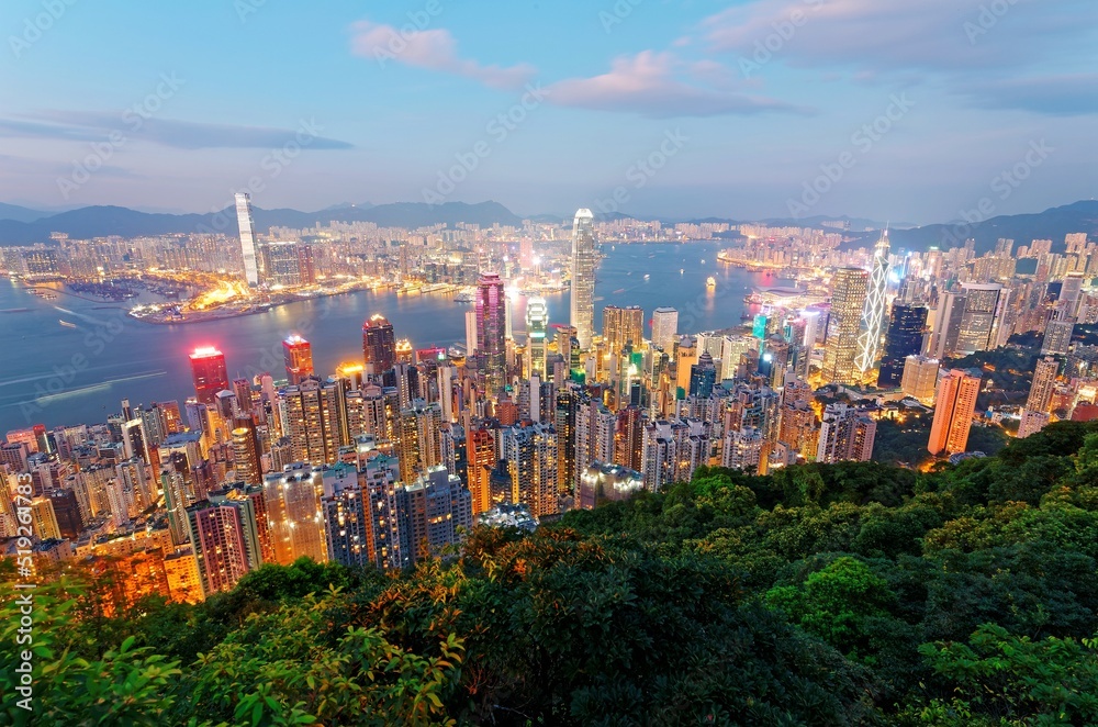 Obraz premium Beautiful city skyline of Hong Kong at night, viewed from top of Victoria Peak, with dazzling lights of crowded modern skyscrapers by Victoria Harbour & Kowloon area across seaport in blue twilight