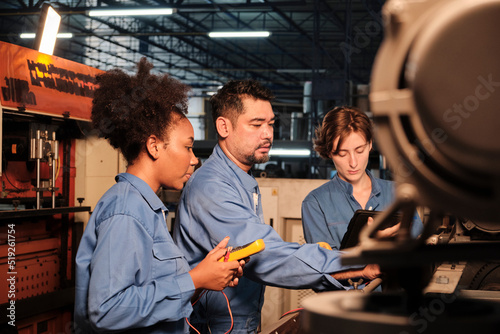 Multiracial professional industry engineer teams in safety uniforms work by inspecting machines' voltage current, checking, and maintaining at manufacture factory, electric system service occupations.