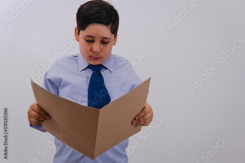 A boy dressed in a suit and tie pretending to be a businessman while reading a folder with important papers. A little boy dressed as a businessman. photo