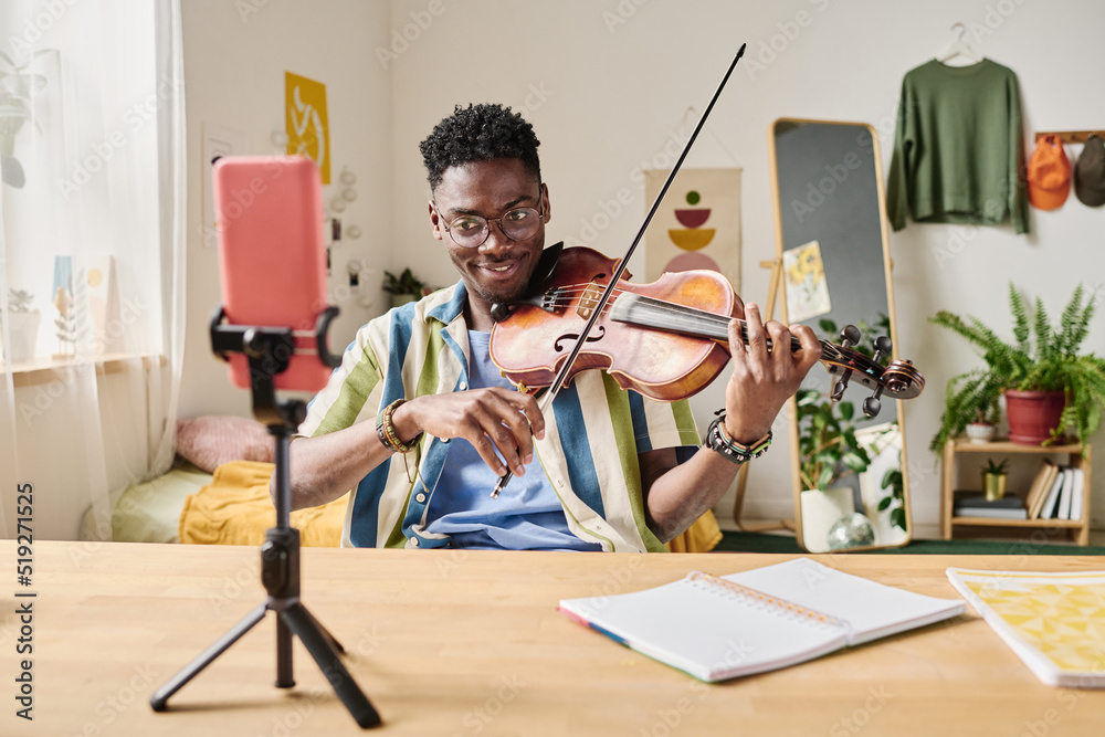 Teen blogger recording video and playing violin for his blog on smartphone on tripod at home Stock | Adobe Stock