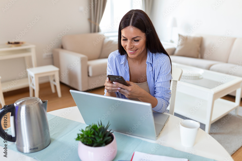 Self employed woman working with her phone and laptop at home. Happy woman using mobile phone while working at home with laptop. Self employed woman working with her phone and laptop at home. Happy woman using mobile phone while working at home with laptop.