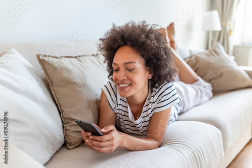 Happy young woman with mobile phone laying on sofa. Beautiful young black women using tablet computer