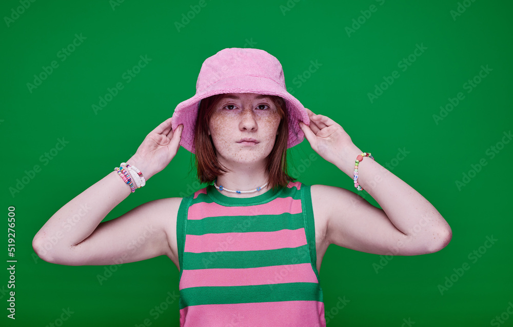 Portrait of teenage girl in pink panama hat looking at camera standing against green background Portrait of teenage girl in pink panama hat looking at camera standing against green background
