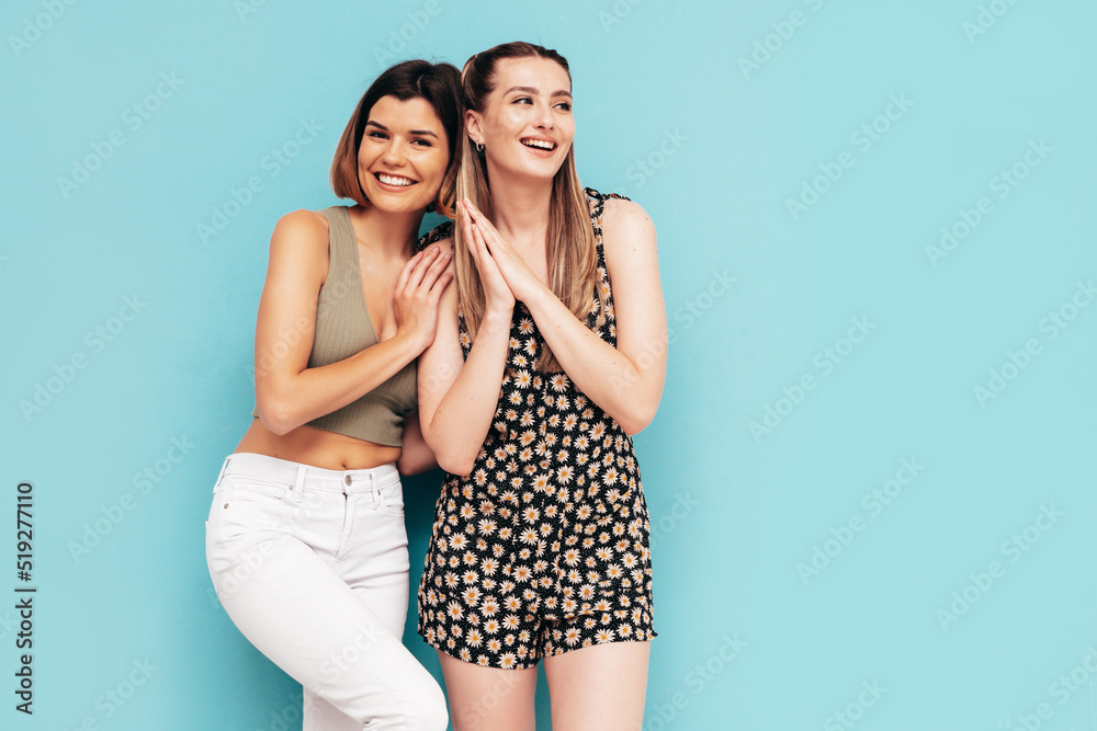 Two young beautiful smiling brunette hipster female in trendy summer clothes. Sexy carefree women posing near blue wall. Positive models having fun. Cheerful and happy. In sunglasses Two young beautiful smiling brunette hipster female in trendy summer clothes. Sexy carefree women posing near blue wall. Positive models having fun. Cheerful and happy. In sunglasses