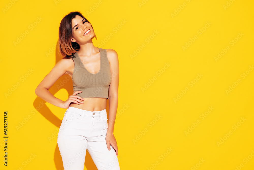 Young beautiful smiling female in trendy summer white jeans clothes. Carefree woman posing near yellow wall in studio. Sexy positive model having fun indoors. Cheerful and happy Young beautiful smiling female in trendy summer white jeans clothes. Carefree woman posing near yellow wall in studio. Sexy positive model having fun indoors. Cheerful and happy