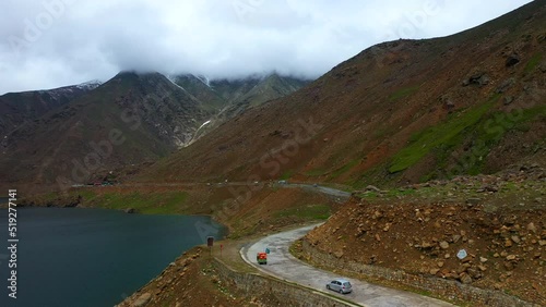 Wide drone shot of a Tuk Tuk on the Babusar pass in Pakistan, with a few vehicles on the road in the Kaghan Valley and a river beside the road photo