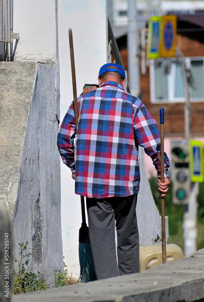 A man cleans the sidewalk on a summer day A man cleans the sidewalk on a summer day