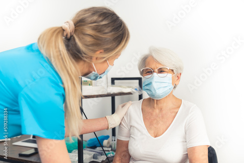 An old woman  with glasses and a protective mask on  smiling to her supportive doctor during a medical checkup in the hospital. High quality photo