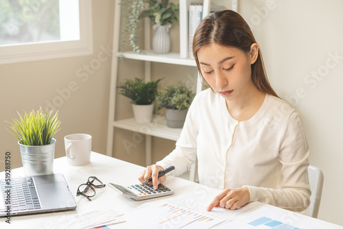 Account finance, attractive asian young business woman hand use calculator for calculate budget, cost and income of company from reports paperwork, plan spend money expenses, working on desk at home.