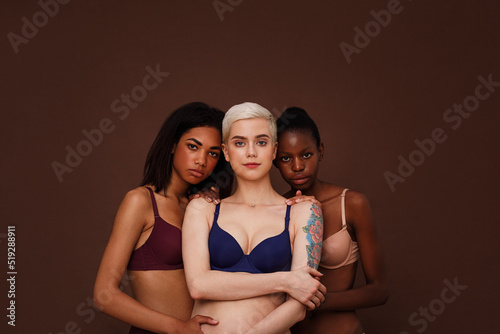 Three women of different skin color standing together. Group of young female in lingerie against backdrop.