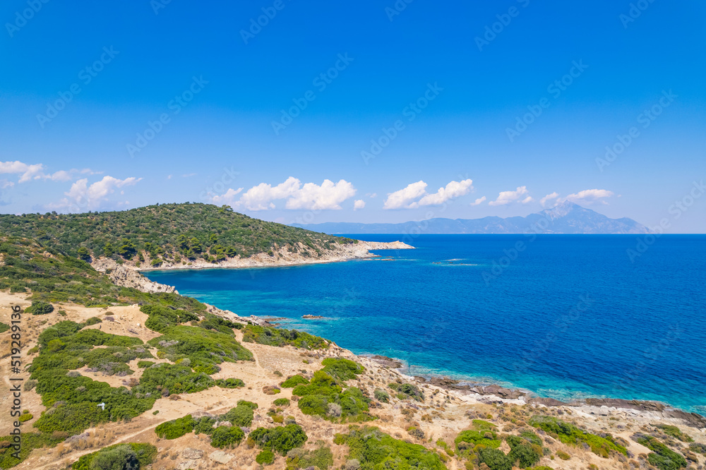 Paralia Acheada, Greece. Beautiful vivid blue and turquoise seashore of a Greek island. Rocky beaches. Amazing weather with blue sky and few fluffy clouds. High quality photo