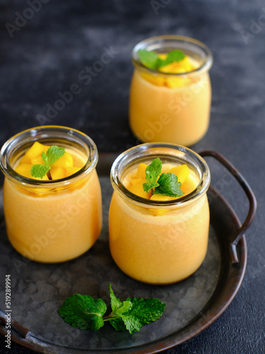 Mango pudding topped with mango chunks and mint leaf garnish. Served in a jar, fresh and healthy
