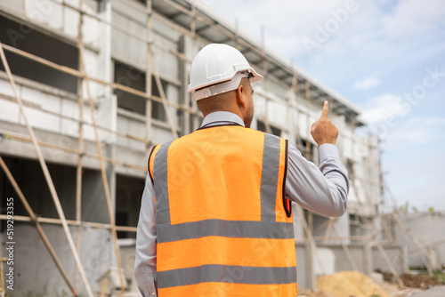 Behind Senior asian engineer man checking and maintenance to inspection at modern home building construction. Architect looking forward with white safety helmet in construction site