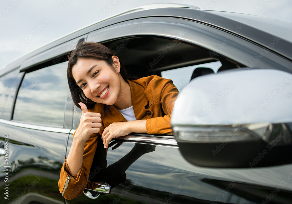 Young beautiful asian women getting new car. she very happy and excited. Smiling female driving vehicle on the road on a bright day. Sticking her head outta the windshield