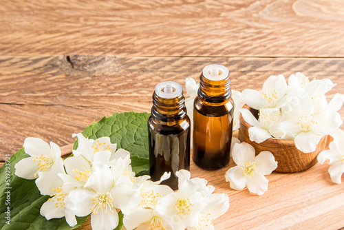 two glass medical bottles of jasmine oil for self-care. the concept of spa and aromatherapy. wooden background with the flowers of the plant.