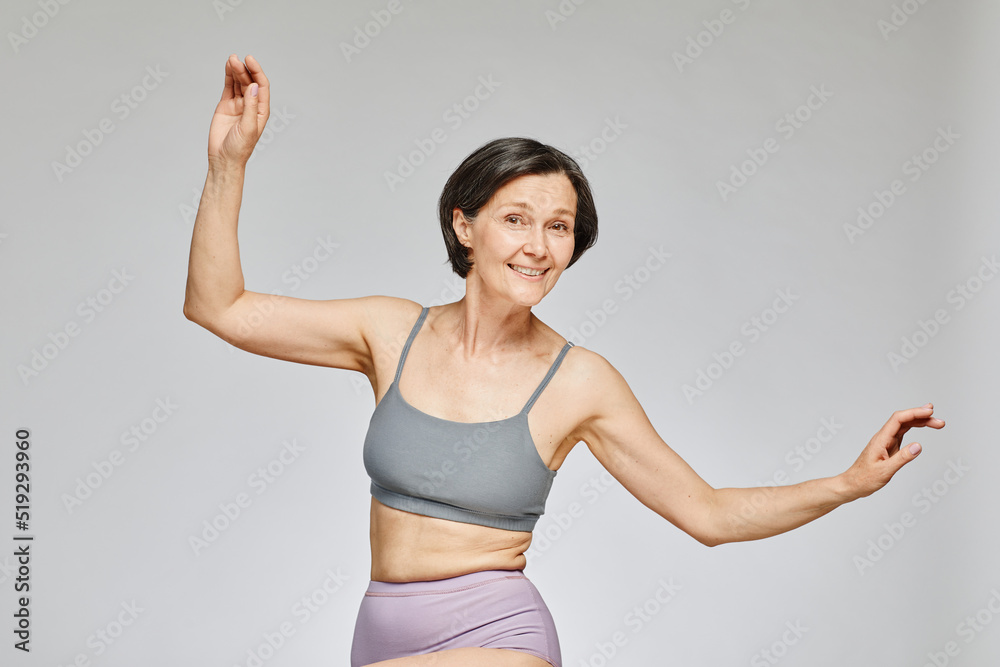 Minimal waist up portrait of carefree mature woman wearing neutral underwear dancing against grey background, body positivity concept, copy space Minimal waist up portrait of carefree mature woman wearing neutral underwear dancing against grey background, body positivity concept, copy space