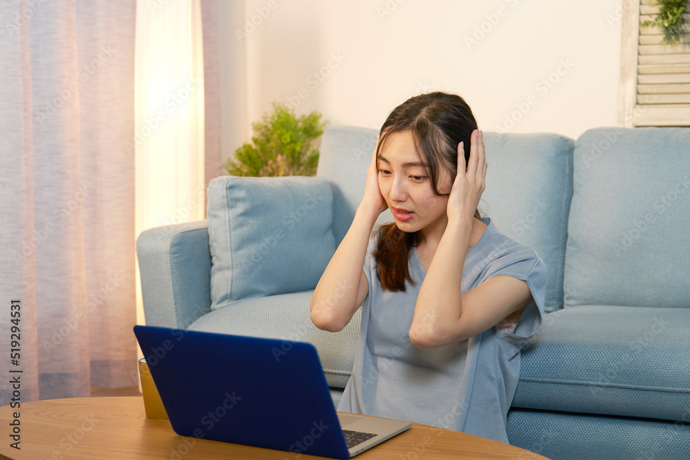 夜にリビングでパソコンを見て頭を抱える女性 夜にリビングでパソコンを見て頭を抱える女性