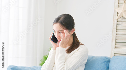 Photos リビングで悩みながらスマホで電話する女性