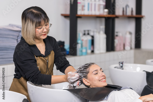 Caucasian young woman get hair washed by hairdresser stylist in salon. Beautiful customer girl lying down on salon washing bed feeling relax and happy enjoy massaging her head at beauty barber shop.